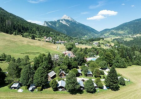 Vue aérienne d’un camping nature Sites et Paysages entouré de montagnes et de forêts, ambiance paisible et verdoyante.
