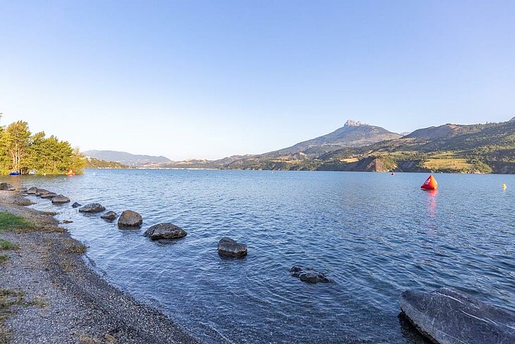 Le plan d’eau d’Embrun près de Baratier, un lieu idéal pour des activités familiales entre baignade, canoë et moments de détente face aux montagnes des Hautes-Alpes.