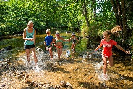 Une animatrice encadrant un groupe d’enfants jouant dans une rivière, illustrant le rôle d’animateur en camping Sites et Paysages pour créer des activités en pleine nature.