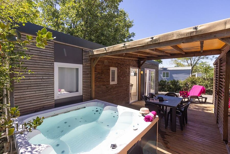 Mobil-home premium climatisé avec terrasse bois, jacuzzi privé et transats pour des vacances grand confort en camping nature.