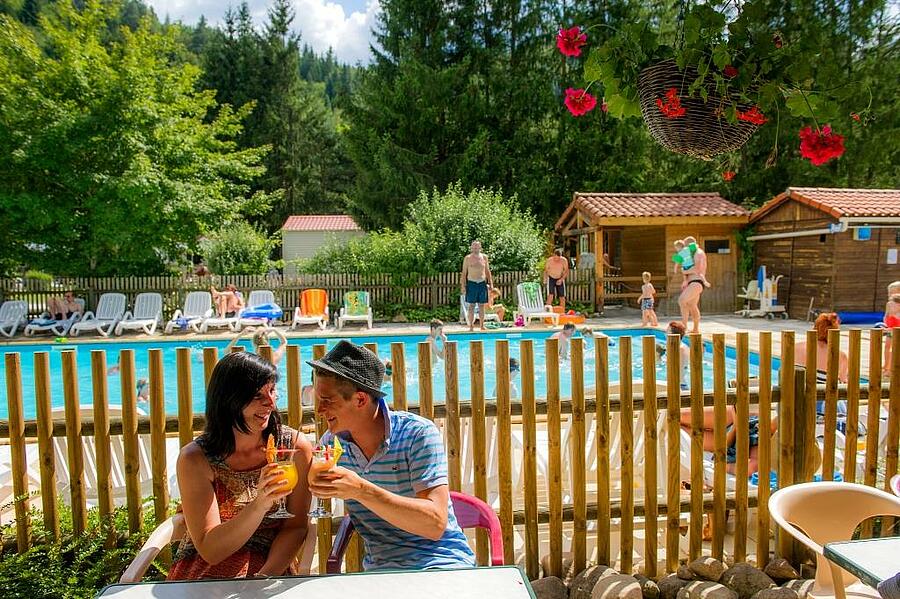 Vacanciers profitant d’un moment convivial autour de la piscine d’un camping en Haute-Loire, entouré de verdure, illustrant l’ambiance chaleureuse et familiale des campings Sites et Paysages.