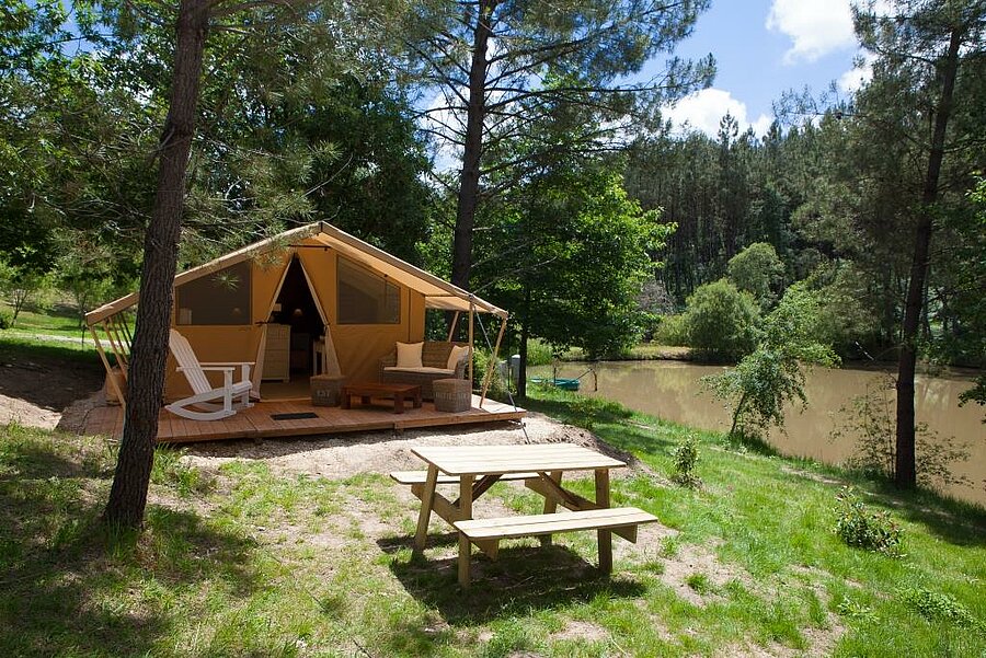 Tente lodge avec terrasse aménagée, situé en pleine nature au bord d’un étang dans un camping du Périgord, en Dordogne.