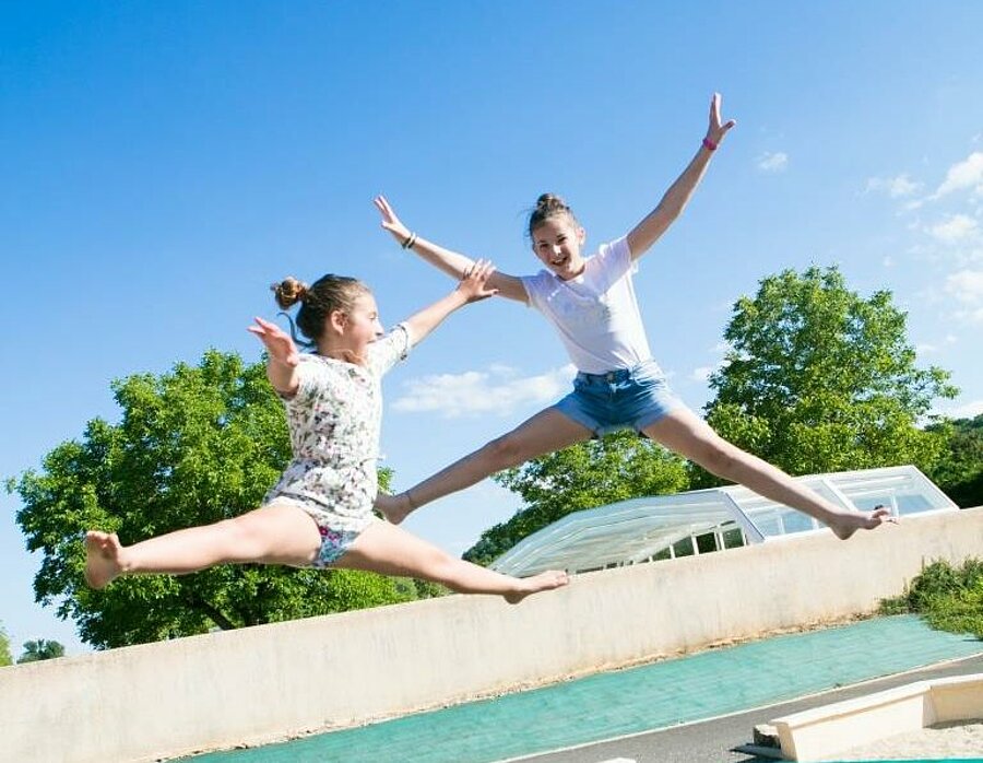 Deux enfants s’amusant sur un trampoline sous le soleil lors d’un week-end de Pâques en camping avec Sites et Paysages, moment de joie et de liberté.