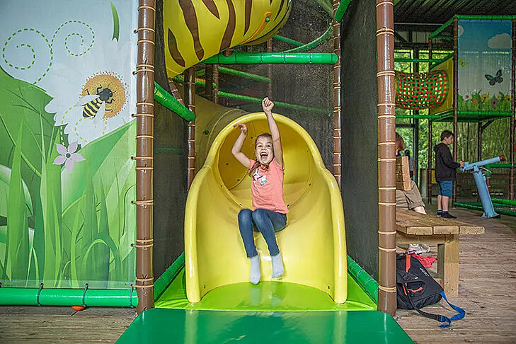 Graines d'Aventures © Terra Botanica Une petite fille descend un toboggan jaune dans l'aire de jeux couverte Graines d'Aventures à Terra Botanica.