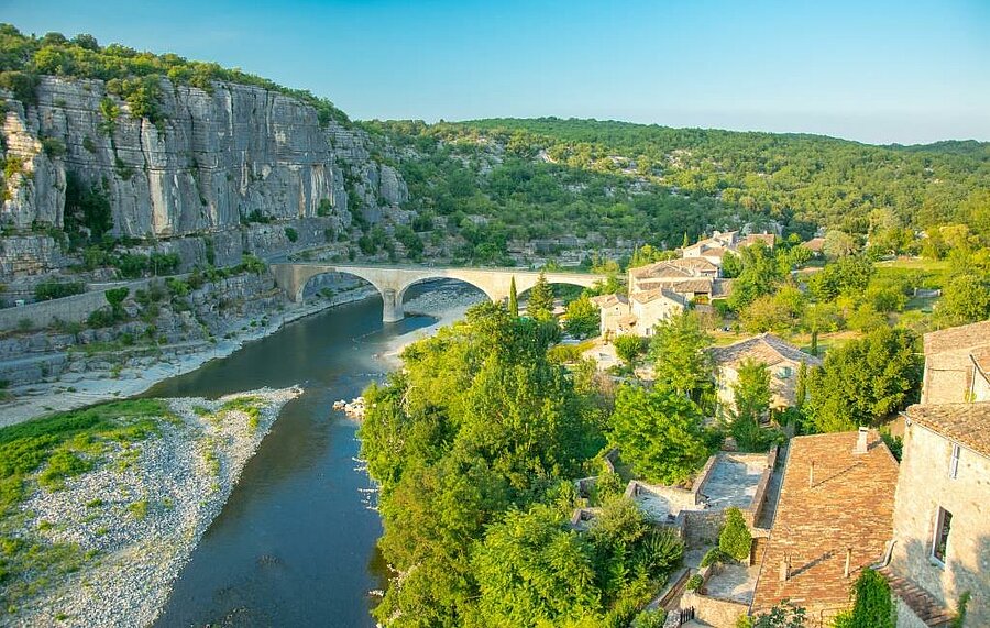 Vue panoramique des Gorges de l'Ardèche avec un pont en pierre et un village typique, Balazuc, entouré de nature, idéal pour des vacances en camping en Auvergne-Rhône-Alpes.