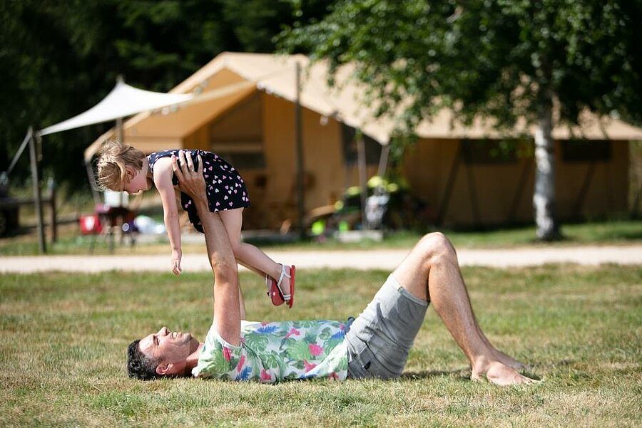 Père jouant avec sa fille devant une tente Lodge dans un camping nature en Haute-Loire, ambiance familiale