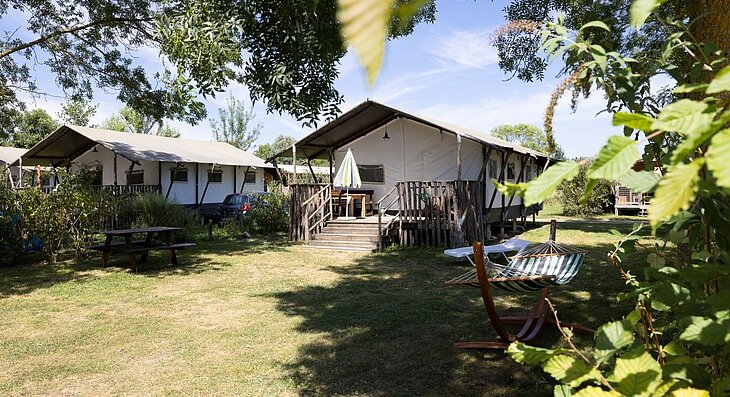 Tente Lodge au Camping L'Étang en Anjou Hébergements sous toile avec terrasses en bois, salon de jardin et hamac au Camping L'Étang, dans un cadre arboré.