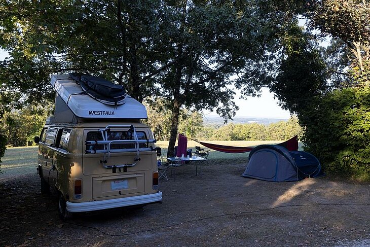 Van et tente à l’ombre des arbres Van, tente et hamac installés sur un emplacement ombragé par de grands arbres