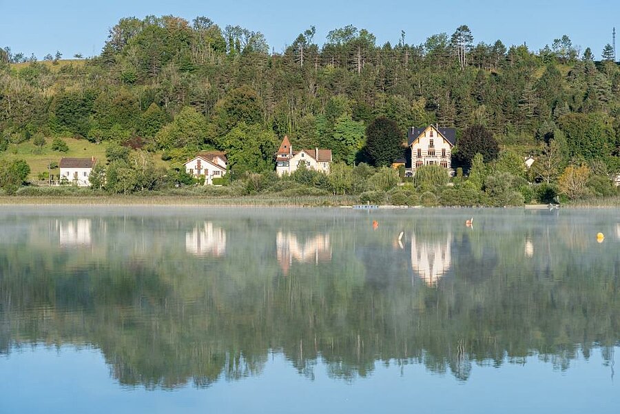 Maisons au bord du lac de Clairvaux, reflets sur l’eau au cœur du Jura, découverte nature et patrimoine local.