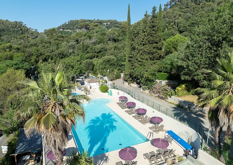 Grande piscine avec transats et parasols au camping 4 étoiles Les Pinèdes, niché dans un cadre verdoyant près de Nice.