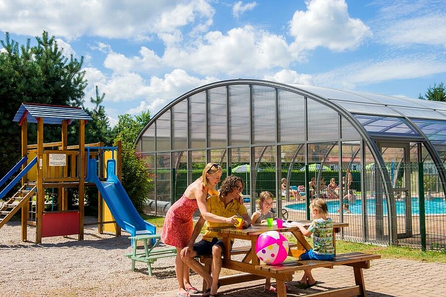 Famille en vacances dans un camping des Vosges avec aire de jeux et piscine couverte, idéale pour des moments de détente avec les enfants