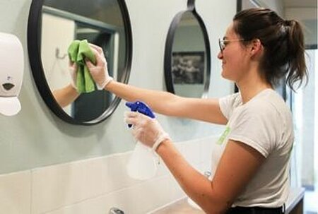 Une agente d'entretien nettoyant un miroir dans un camping Sites et Paysages, illustrant le poste essentiel d’agent d’entretien pour garantir un environnement propre et accueillant.