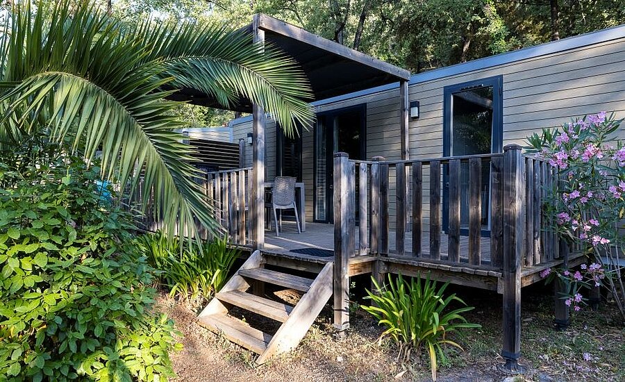 Mobil home moderne avec terrasse boisée et végétation méditerranéenne, parfait pour une location de mobil home en camping en France.