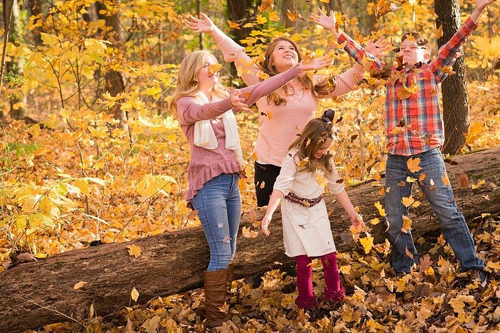 Famille jouant avec les feuilles mortes en forêt, éclats de rire et couleurs d’automne.