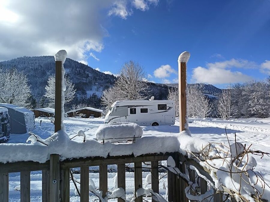 Camping caravaneige sous la neige avec un camping-car stationné face aux montagnes enneigées. Un cadre idyllique pour profiter des joies de l’hiver en pleine nature.