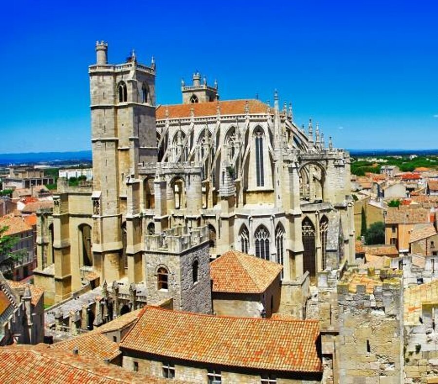 Panorama sur la cathédrale de Narbonne et les toits ocres de la ville sous un ciel bleu éclatant, emblématique du Languedoc-Roussillon.