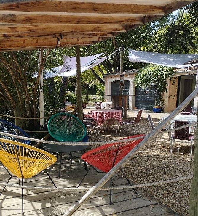 Terrasse ombragée du Camping Domaine de l’Écluse Terrasse ombragée avec tables et fauteuils colorés au Camping Domaine de l’Écluse à Bénivay-Ollon.
