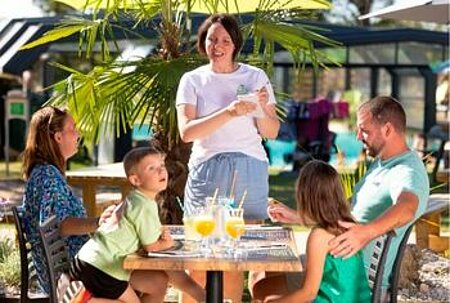 Une serveuse prenant la commande d'une famille sur la terrasse d’un camping Sites et Paysages, illustrant le poste de serveur dans un cadre convivial et naturel.