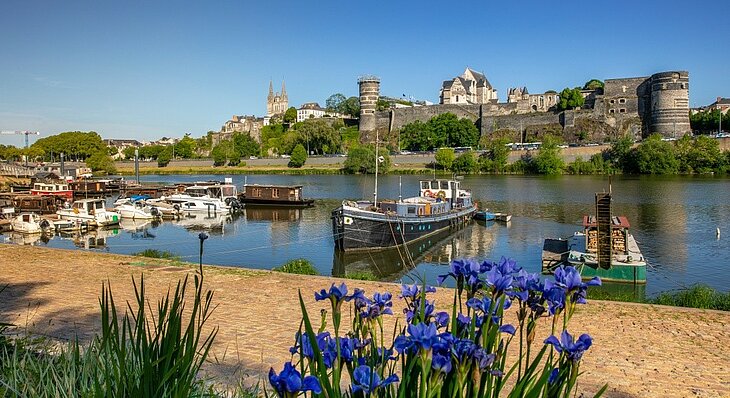 Le château d'Angers et ses remparts Vue sur les remparts et les tours du château d'Angers dominant la Maine, avec des bateaux amarrés au premier plan.