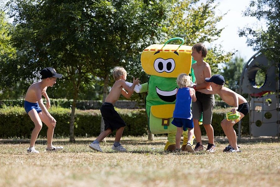 Enfants jouant avec Pako, la mascotte du camping L’Étang, lors d’une animation en plein air dans un cadre arboré près d’Angers.