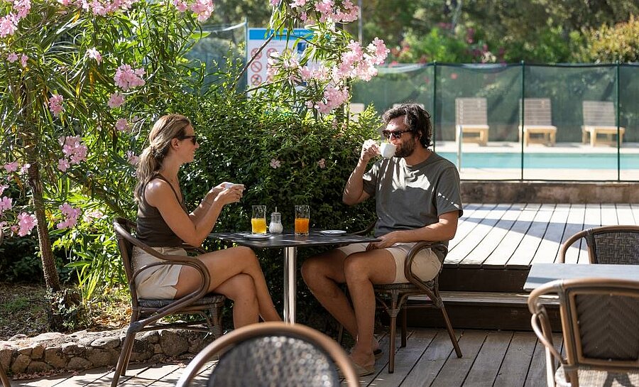 Couple prenant un café en terrasse fleurie près de la piscine d’un camping à côté de Porto-Vecchio, ambiance détente et nature.