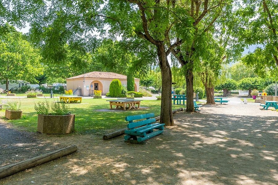 Aire ombragée avec bancs et tables de pique-nique dans un camping des Alpes-de-Haute-Provence, idéale pour des vacances en famille au cœur de la nature.
