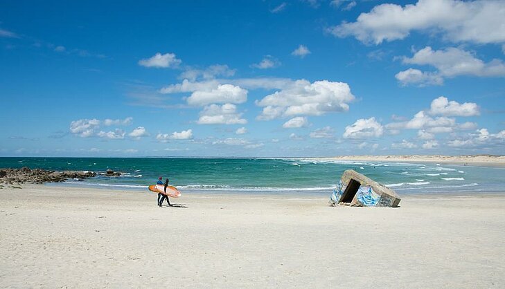Surfeur marchant sur la plage de la Pointe de la Torche, côte sauvage du Finistère, symbole nature et liberté du Finistère Tourisme.