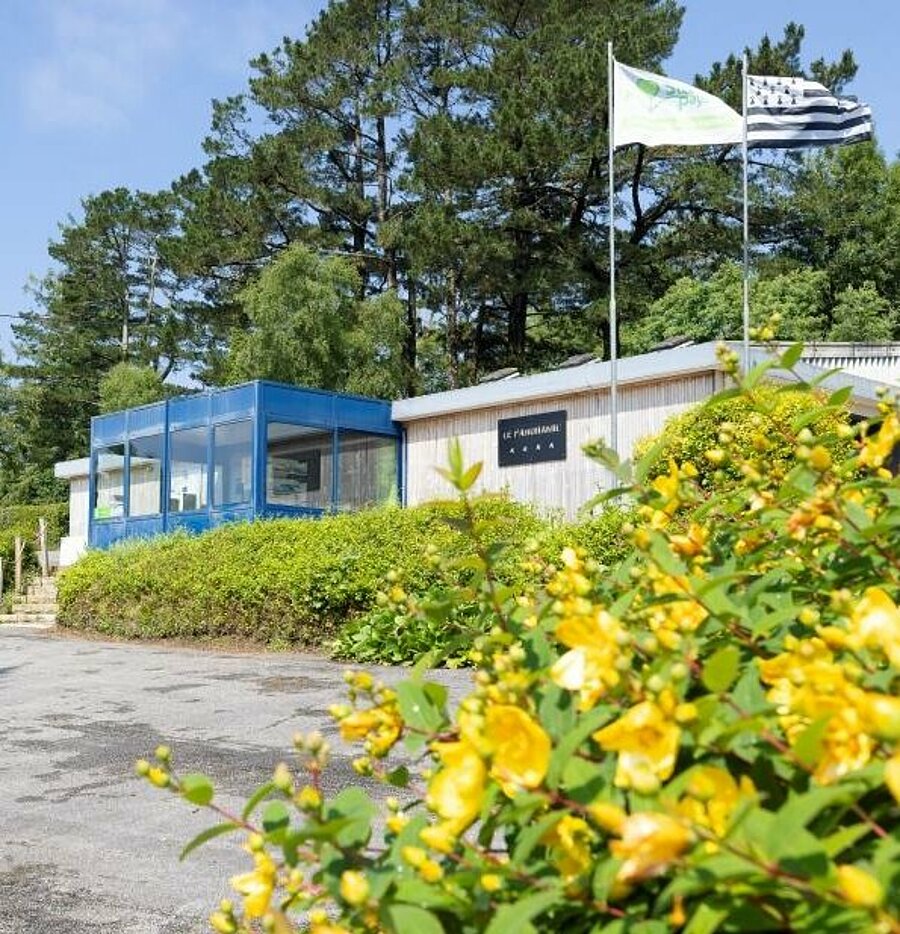 Accueil fleuri d'un camping dans le Finistère, avec le drapeau breton flottant fièrement au vent, parfait pour des vacances en pleine nature en Bretagne.