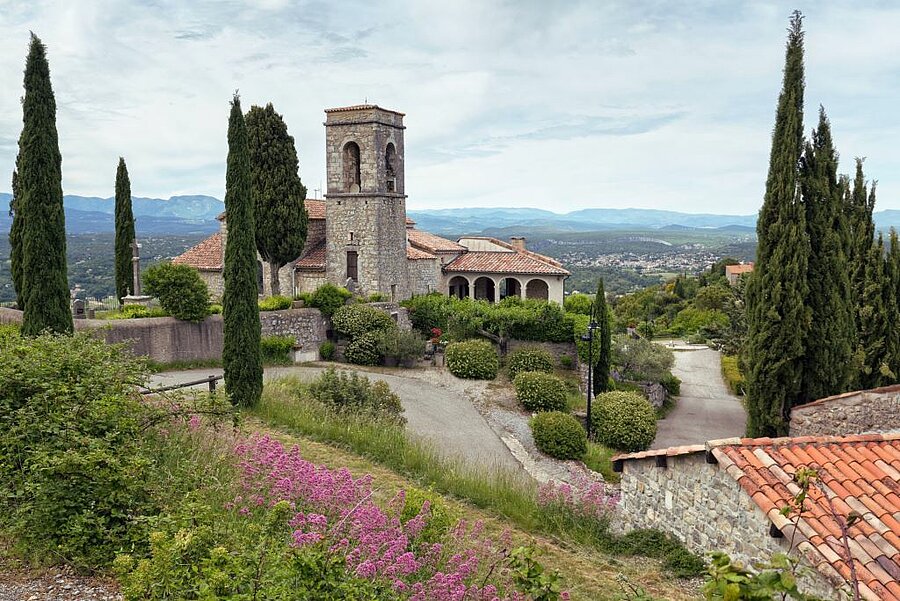 Vue sur l’église Saint-Martin de Sampzon et la vallée ardéchoise, entourée de cyprès et de collines verdoyantes.
