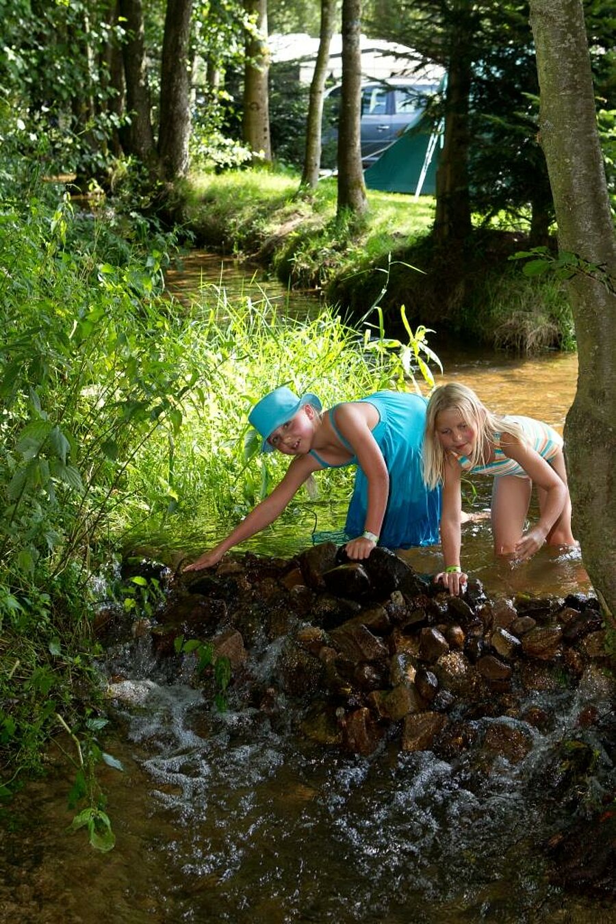 Enfants jouant dans un ruisseau en pleine nature près de leur tente, expérience authentique pour un week end famille au camping.