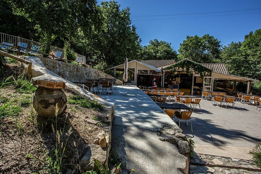 Terrasse ombragée d’un restaurant dans un camping près d’Aubenas, idéale pour se détendre et profiter des vacances en pleine nature.