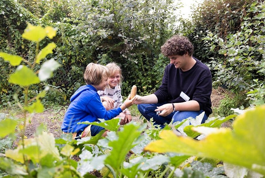 Deux enfants découvrent un légume du potager en compagnie d’un animateur dans un camping écolabel, illustrant l’engagement écologique du site.