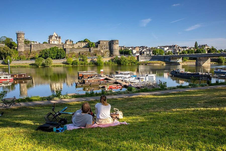 Couple assis sur la pelouse avec vue sur le château d’Angers et les bateaux de la Maine, à deux pas d’un camping de la région.