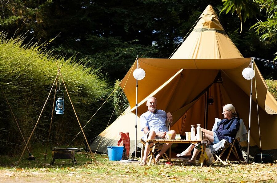 Couple installé devant une tente atypique dans un camping au cœur des Côtes d’Armor, pour un séjour nature et confortable en Bretagne