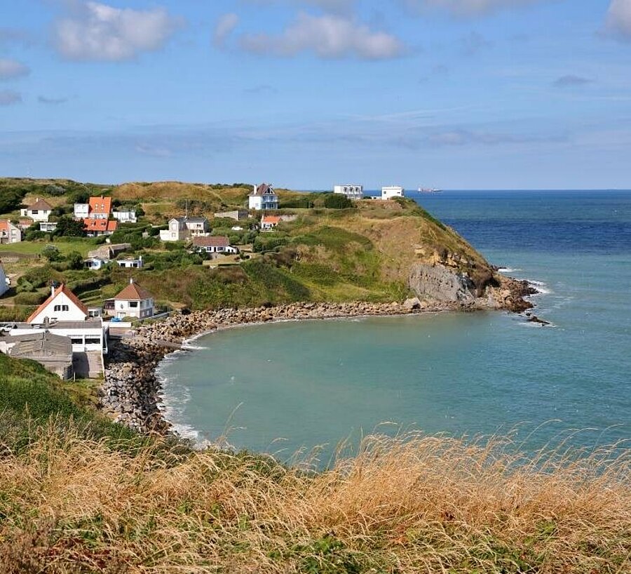 Vue sur une baie pittoresque et un village typique de la Côte d’Opale, avec ses falaises verdoyantes et ses maisons en bord de mer, parfait pour des vacances en camping.