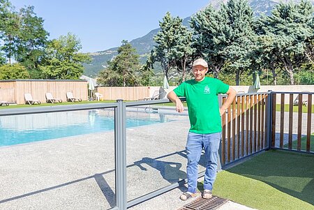 Franck, propriétaire du camping Sites et Paysages Le Petit Liou dans les Hautes-Alpes, près de la piscine de son établissement, avec les montagnes en arrière-plan.