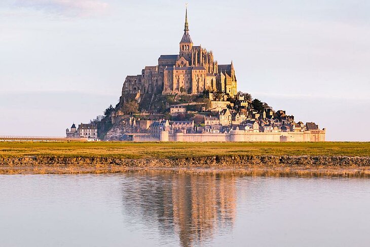 Visiter le Mont-Saint-Michel Vue du Mont-Saint-Michel en Normandie au coucher du soleil, abbaye majestueuse et reflets sur les prés salés, visite incontournable pour retraités.