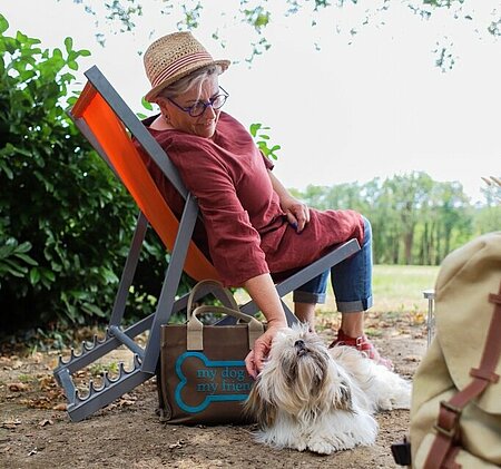 Femme détendue en transat caressant son chien, dans un camping à taille humaine où les animaux sont acceptés.
