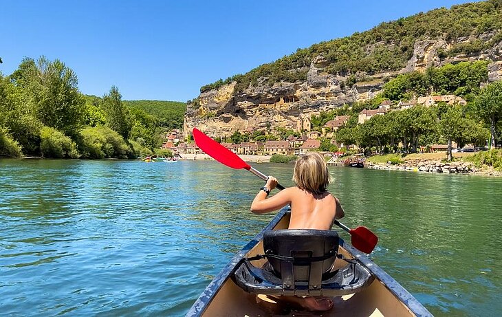 Enfant en canoë sur la Dordogne près d’un village du Périgord, activité phare du tourisme en Nouvelle-Aquitaine.