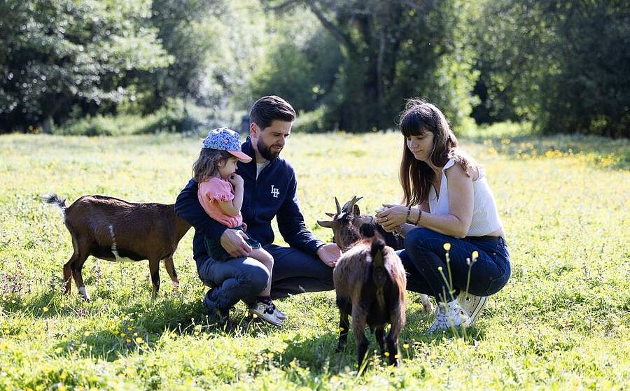 Une famille en vacances dans un camping en Normandie interagissant avec une chèvre dans un mini parc animalier, entourée d’un cadre naturel verdoyant.