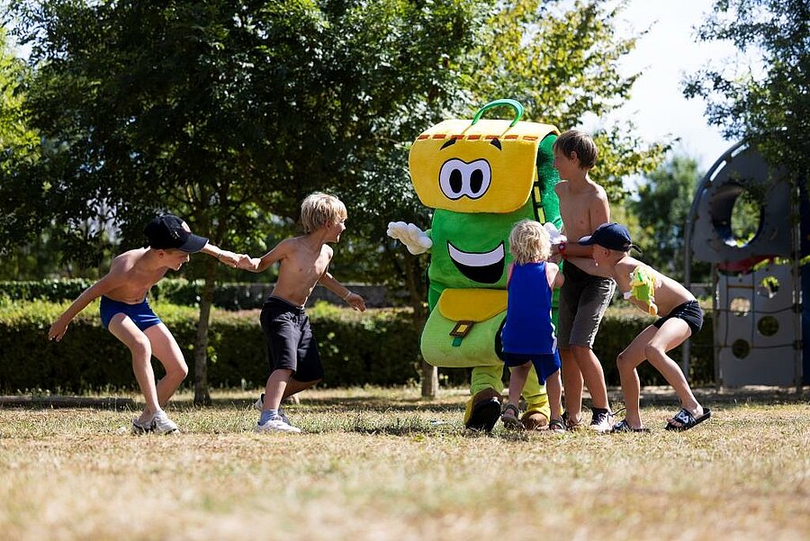Groupe d’enfants jouant avec Pako, la mascotte souriante dans un camping familial des Pays de la Loire, ambiance conviviale.