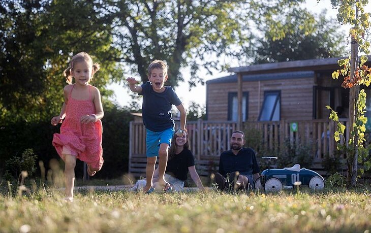 Le camping, l’allié des vacances famille petit budget Enfants jouant devant un mobil-home en camping familial, idéal pour des vacances famille petit budget.