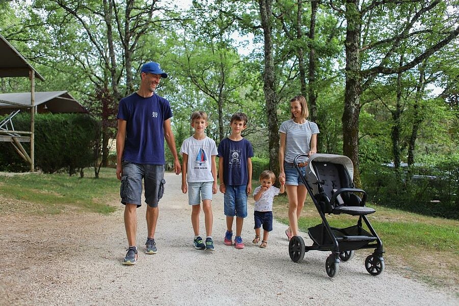 Famille avec enfants et poussette se promenant dans un camping arboré, cadre paisible idéal pour un week end famille.