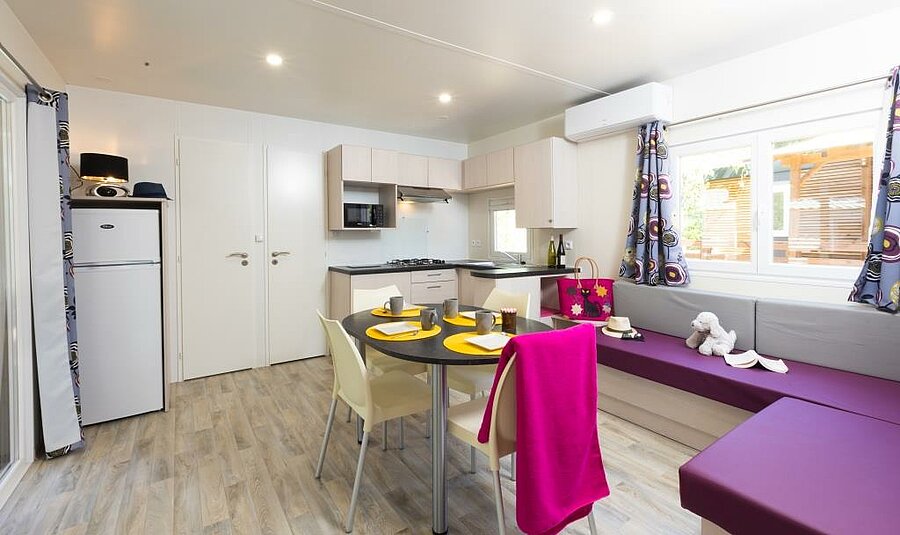 Salon et cuisine d’un mobil-home climatisé, parfait pour des vacances au frais en famille même en pleine canicule.