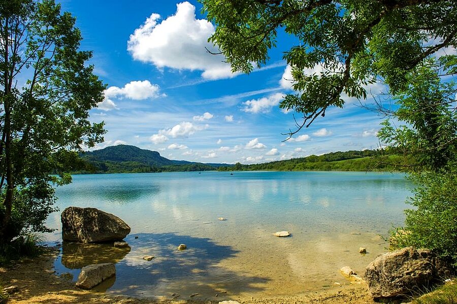 Lac aux eaux claires bordé d’arbres, sous un ciel bleu, dans le Jura, idéal pour des vacances nature en camping en Bourgogne-Franche-Comté.