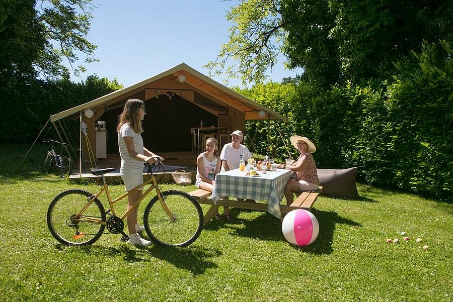 Famille partageant un repas devant une tente de camping.