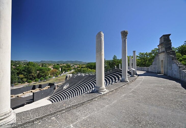 Le théâtre antique Théâtre antique de Vaison-la-Romaine avec ses gradins et colonnes, sous un ciel bleu avec les reliefs en arrière-plan.