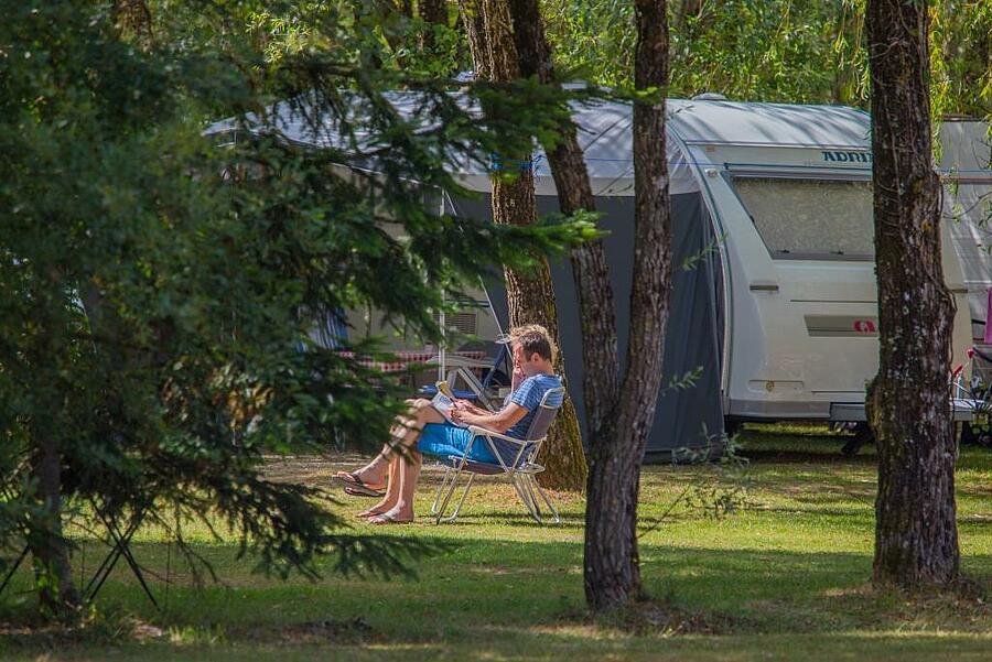 Vacanciers se relaxant devant leur caravane sur un emplacement ombragé et verdoyant dans un camping du Loir-et-Cher, idéal pour un séjour au calme en pleine nature.