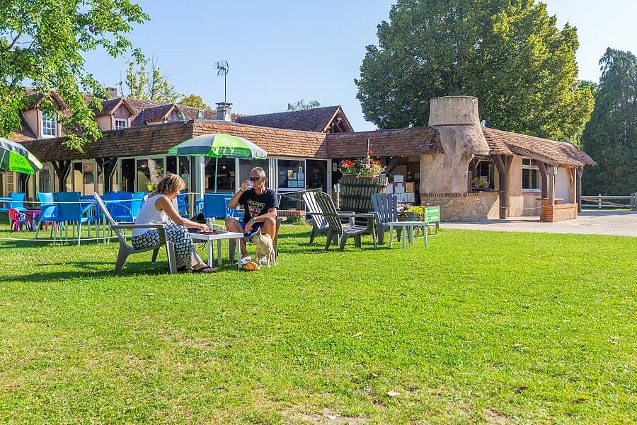 Couple profitant d’un moment de détente en plein air sur la pelouse d’un camping dans le Loir-et-Cher, avec des tables et chaises colorées, idéal pour des vacances conviviales en famille.