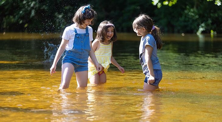 Se rafraîchir dans une rivière en été Trois enfants jouent et se rafraîchissent dans une rivière pendant une journée d’été.